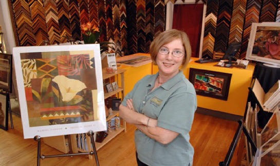 Sheri Cox standing in the front room gallery next to a modern art print on an easel