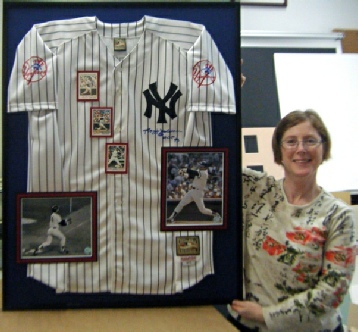 lady holding a shadowbox frame with autographed Yankees framed Yankees and pictures player's uniform shirt.